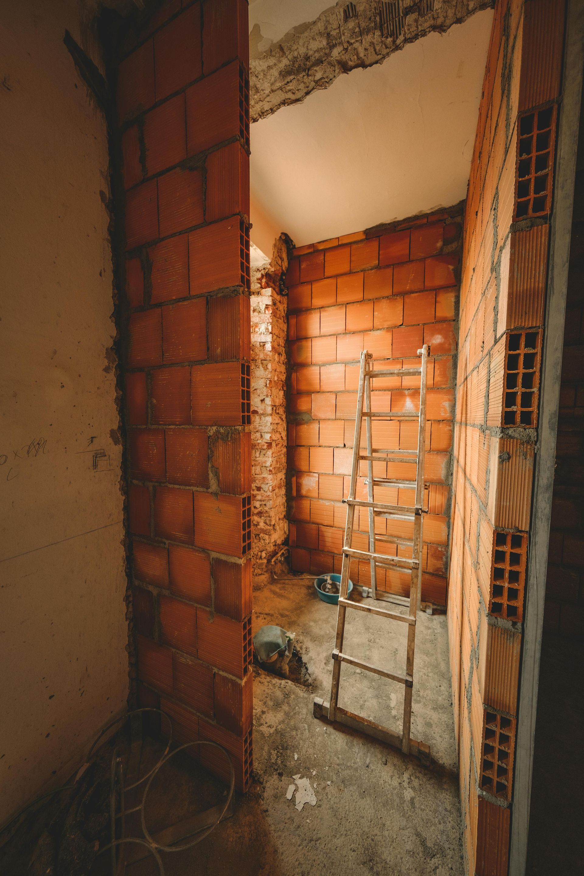 Interior view of a construction site with exposed brick walls, a ladder, and tools on the floor.