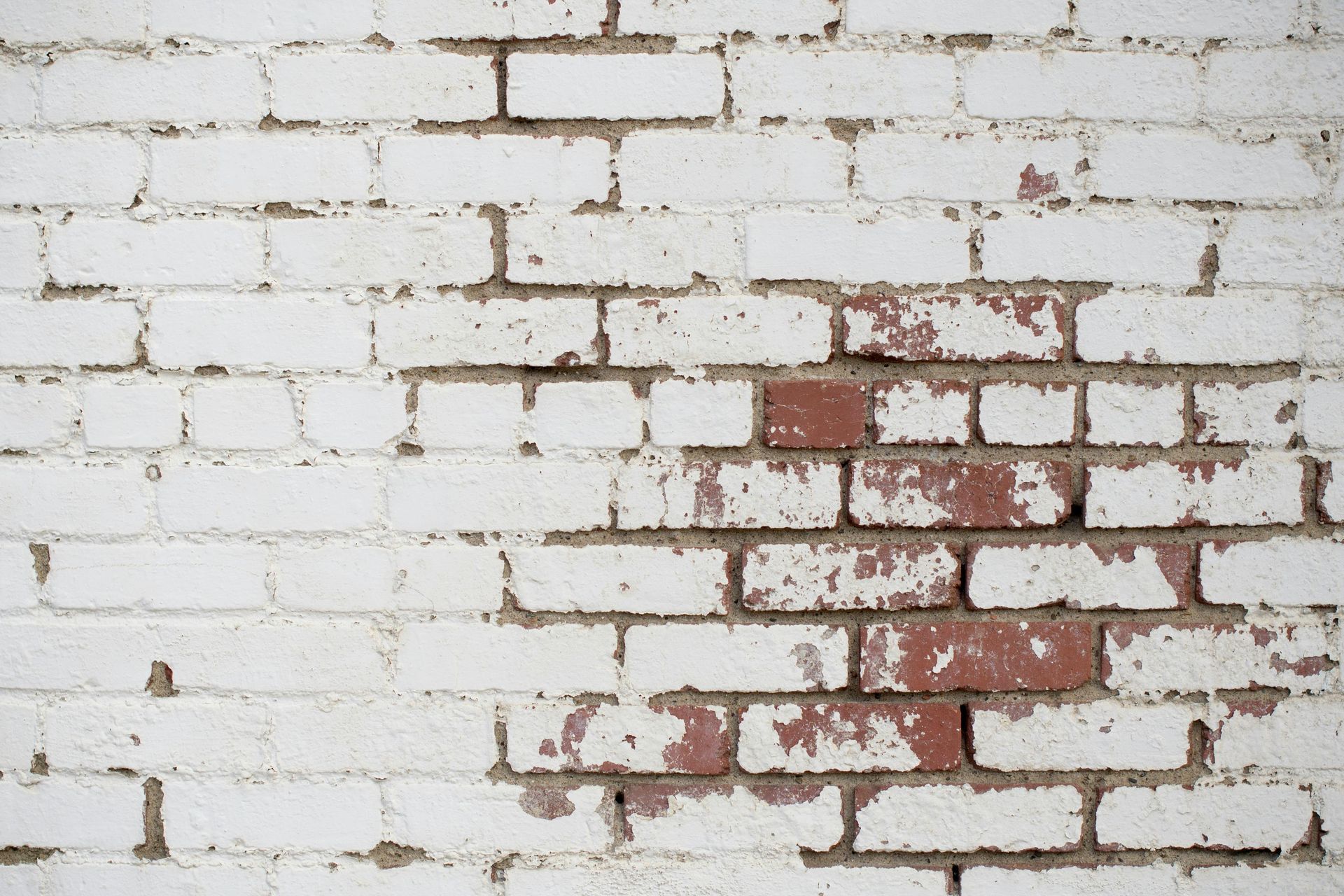 White-painted brick wall with sections of chipped paint revealing the red brick underneath.