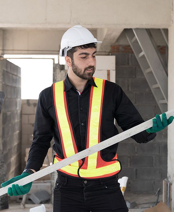 Construction worker wearing a safety vest and helmet, inspecting a white beam.