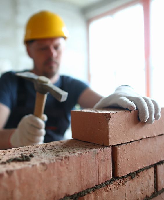 Bricklayer in a yellow hard hat, laying bricks with a hammer, building a wall.