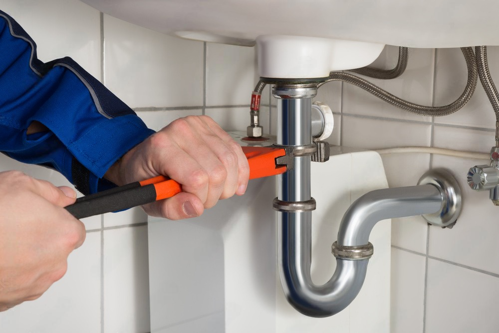 a plumber is fixing a sink pipe with a wrench .