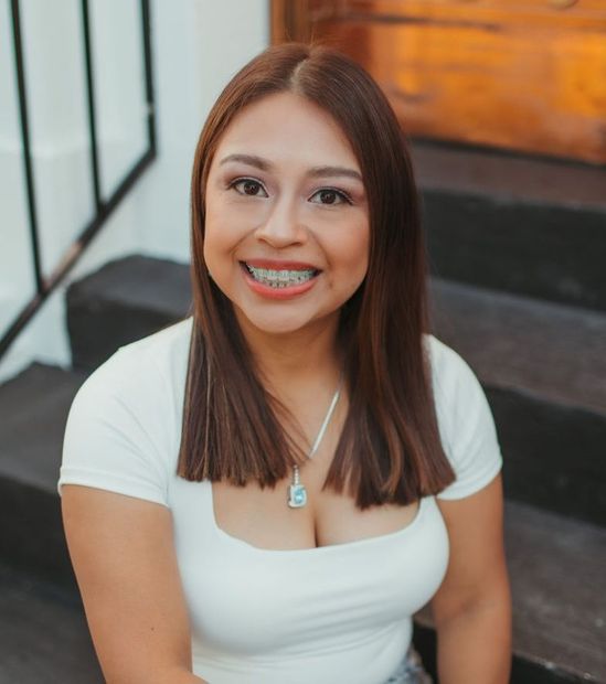 A woman is sitting at a desk with a laptop and a vase of flowers.