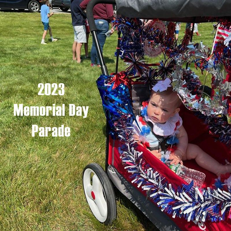 Beautiful baby wearing red, white and blue and sitting in a decorated wagon at the Memorial Day parade.