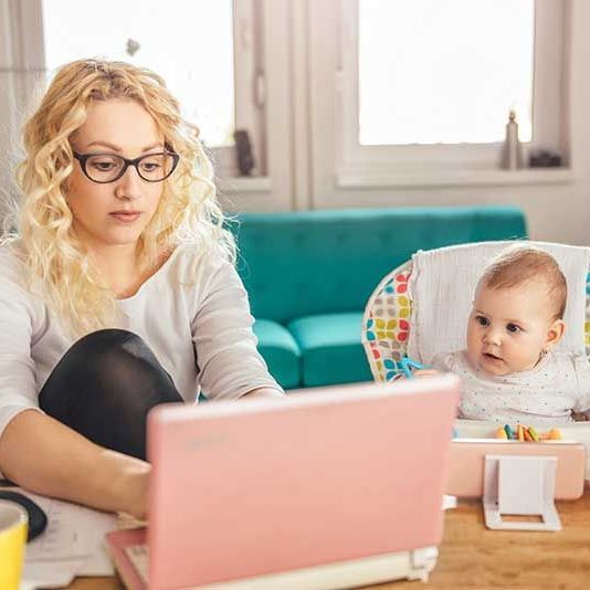 Mom on a laptop with baby in a highchair