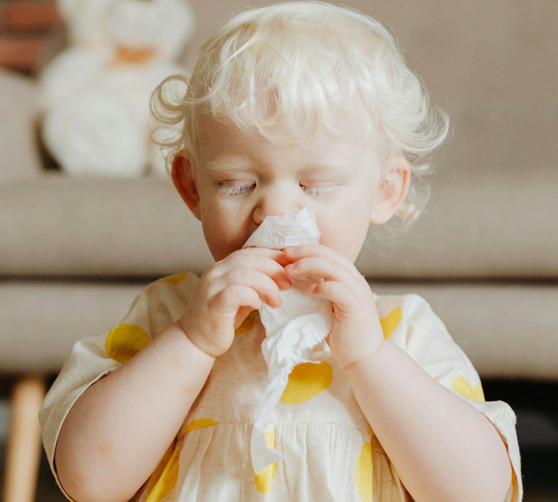 A little girl is blowing her nose with a napkin.