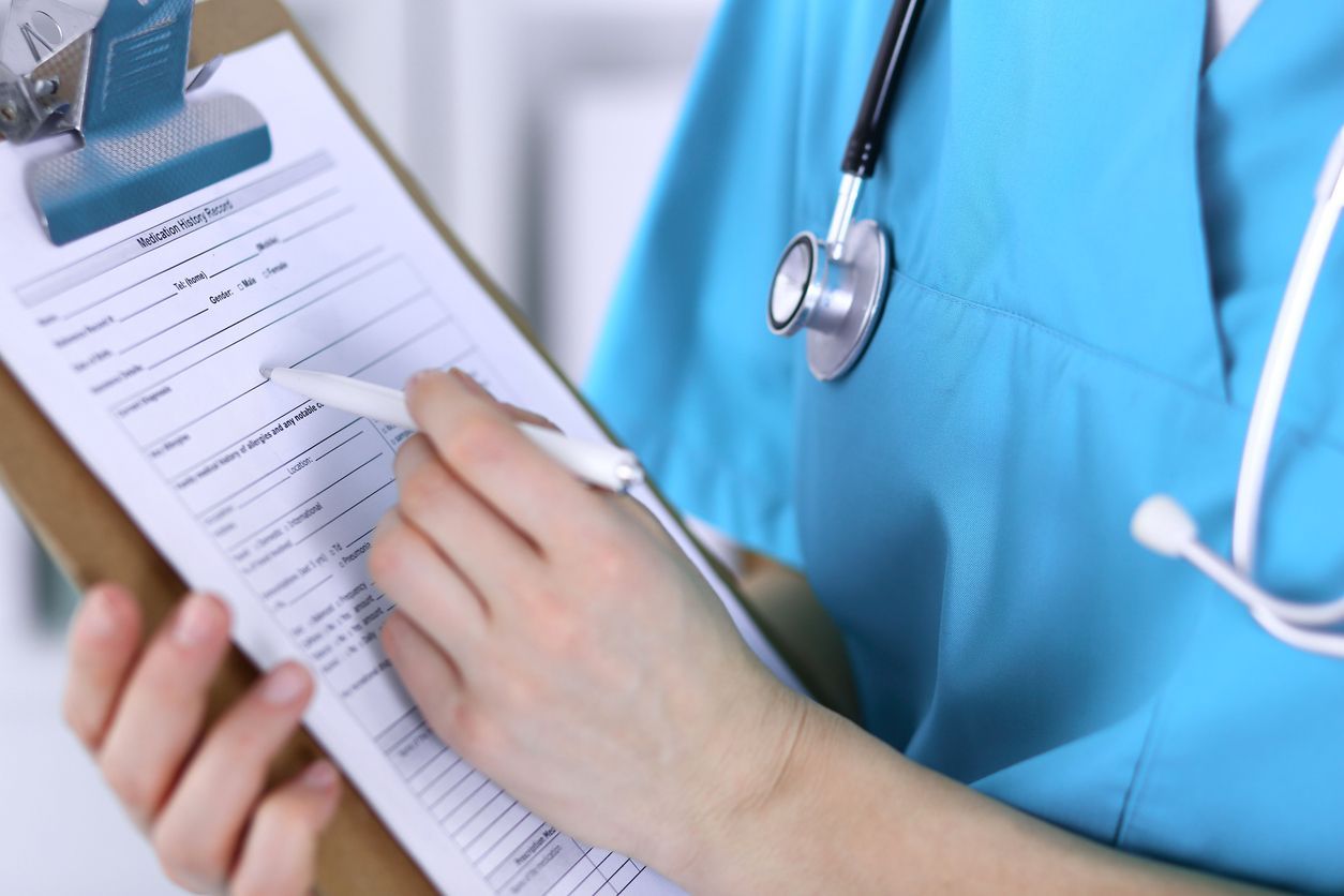 A nurse is writing on a clipboard with a pen.