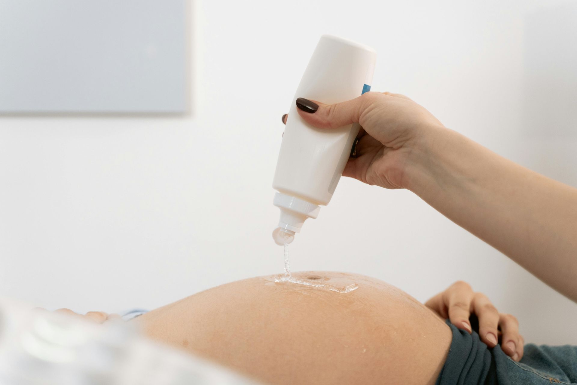 A woman is applying lotion to a pregnant woman 's belly.