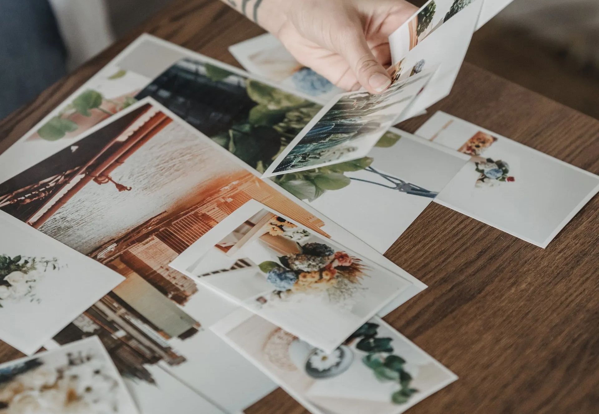 a person is holding a picture over a pile of pictures on a wooden table .