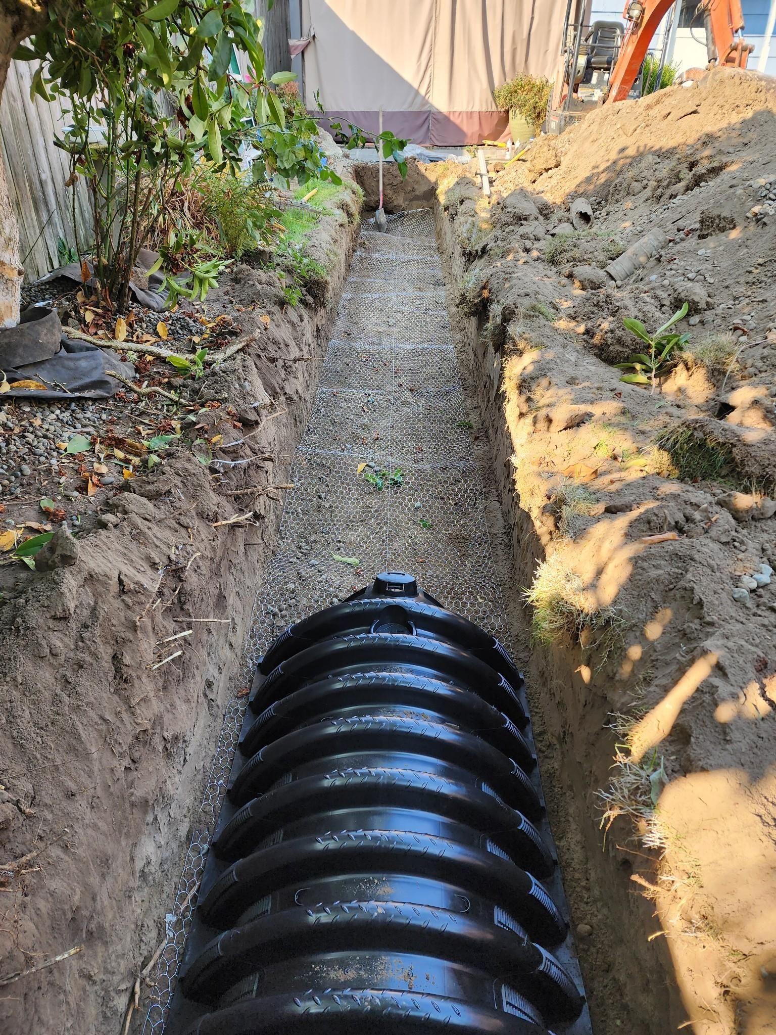 A large black pipe is being installed in a trench.