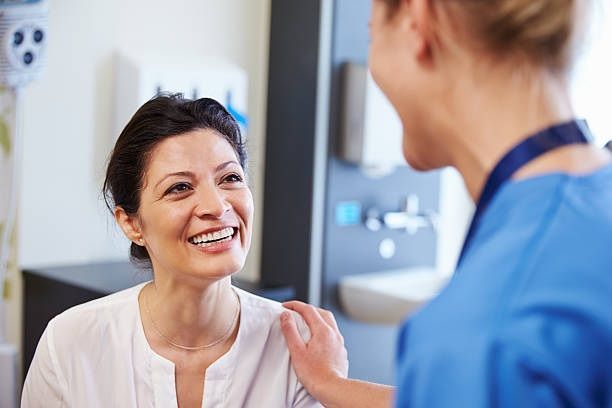 Smiling patient talks with a clinician in a medical office, with the clinician’s hand on her shoulder.