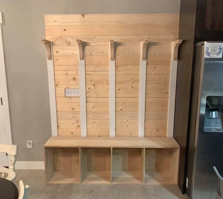 A wooden bench is sitting in a room next to a refrigerator.