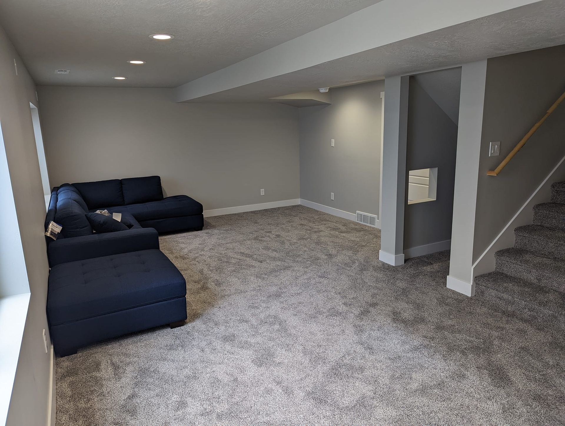 A living room in a basement with a blue couch and stairs.