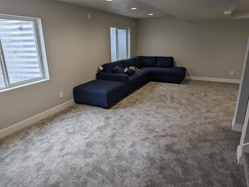 A living room with a blue sectional couch and a gray carpet.