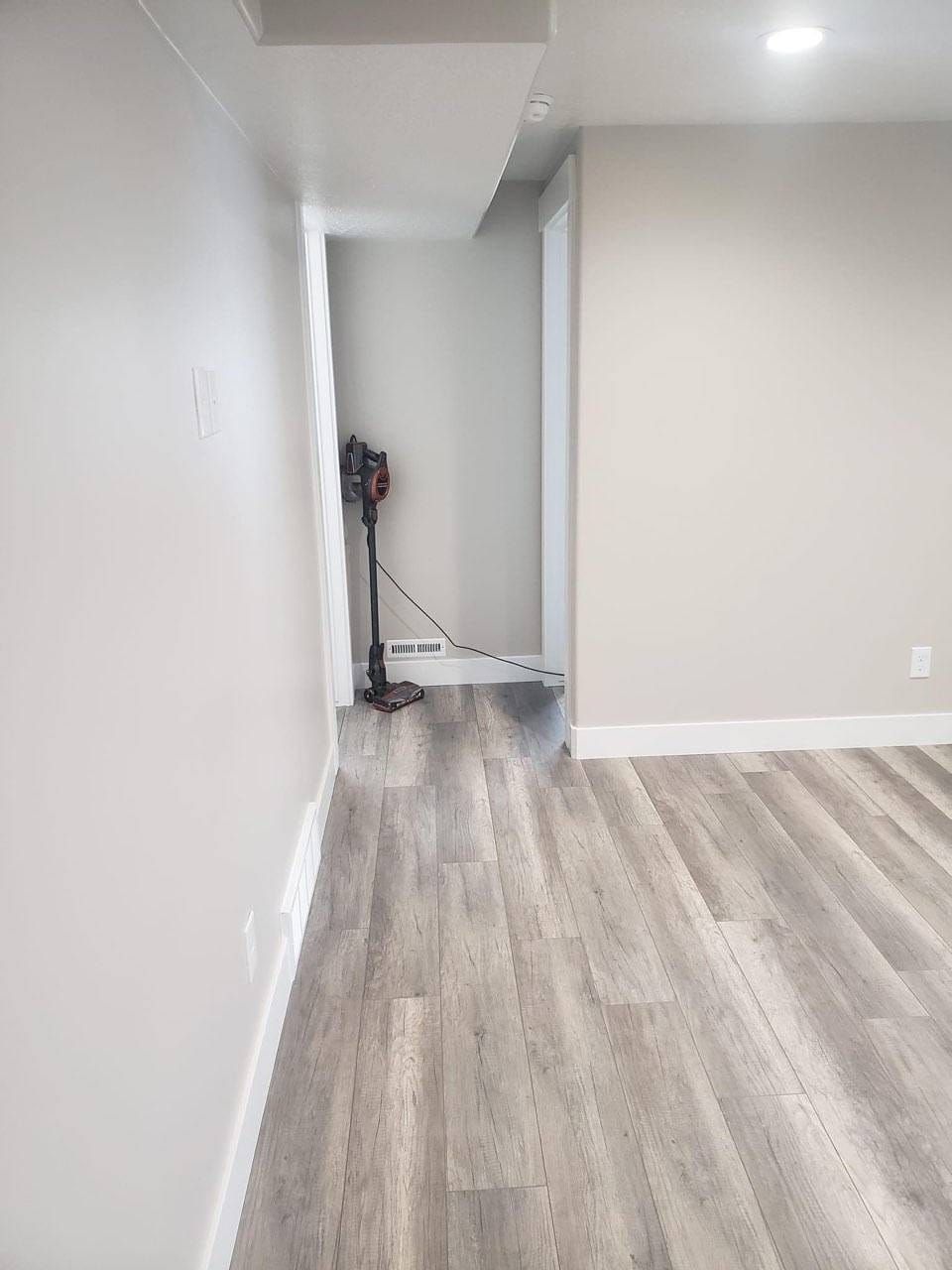 An empty basement with hardwood floors and white walls.