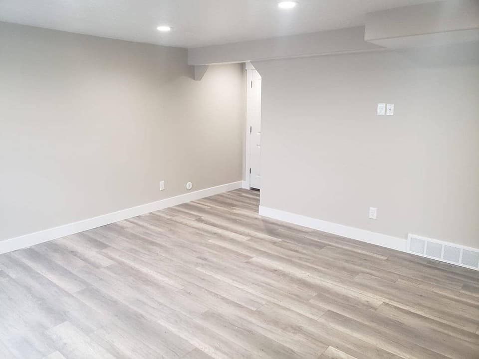 An empty basement with hardwood floors and white walls.