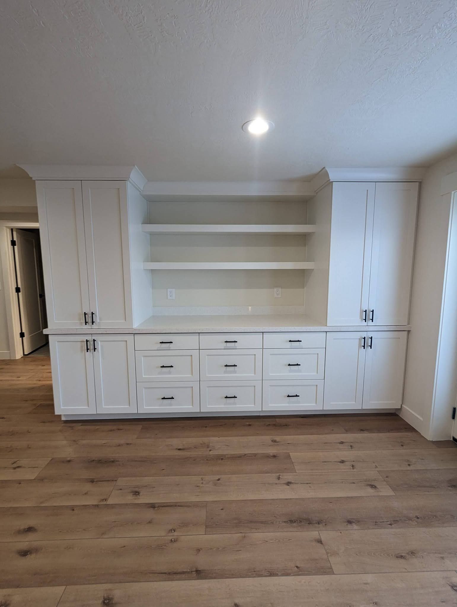 A large empty room with hardwood floors and white cabinets.