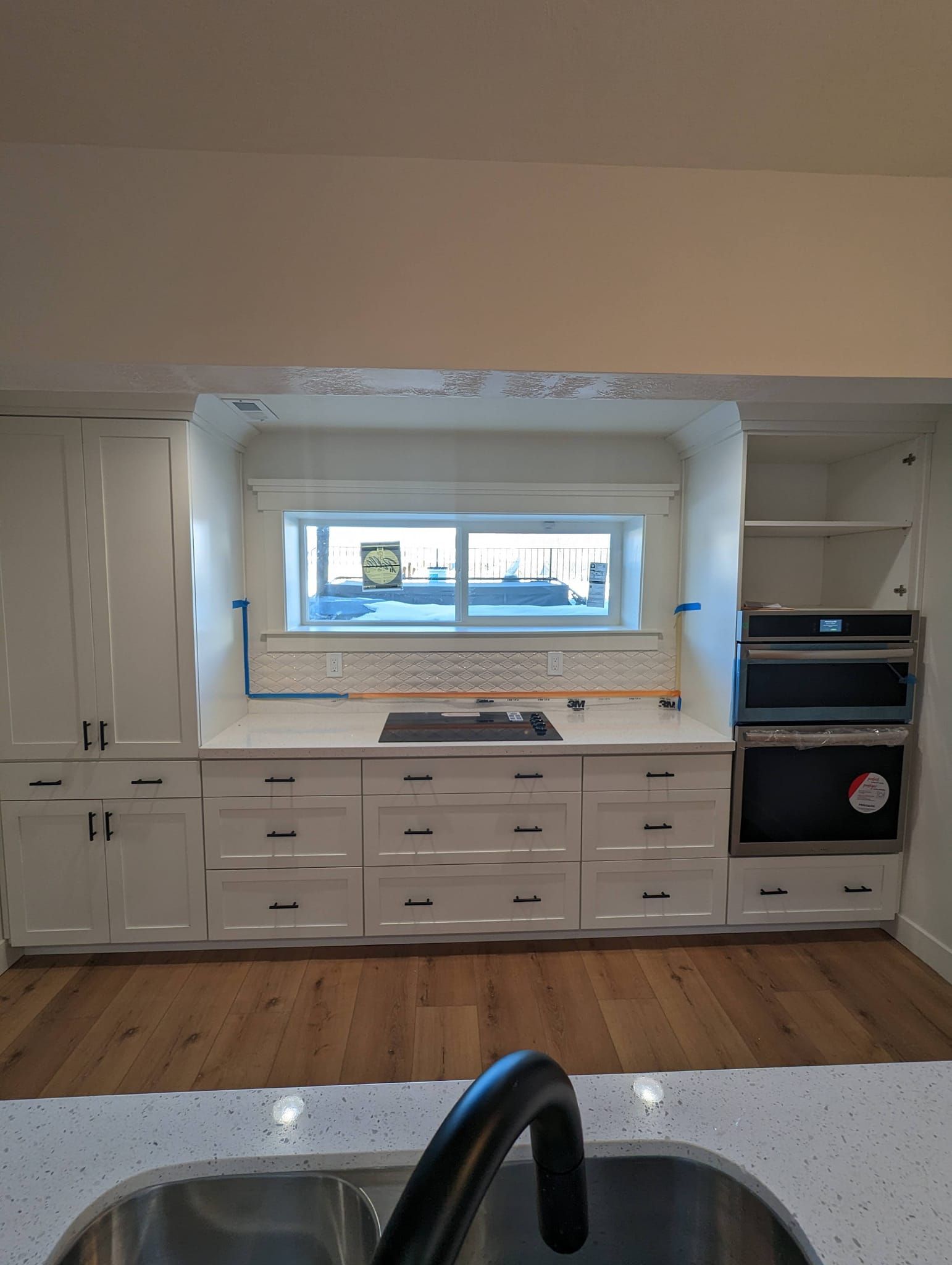 A kitchen with white cabinets , stainless steel appliances , a sink , and a window.