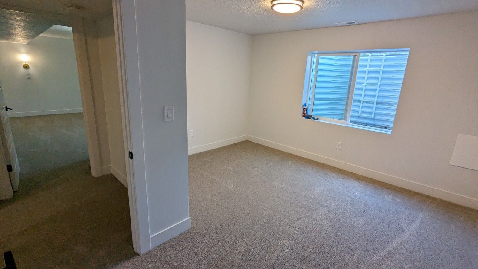 An empty room with a large window and a carpeted floor.