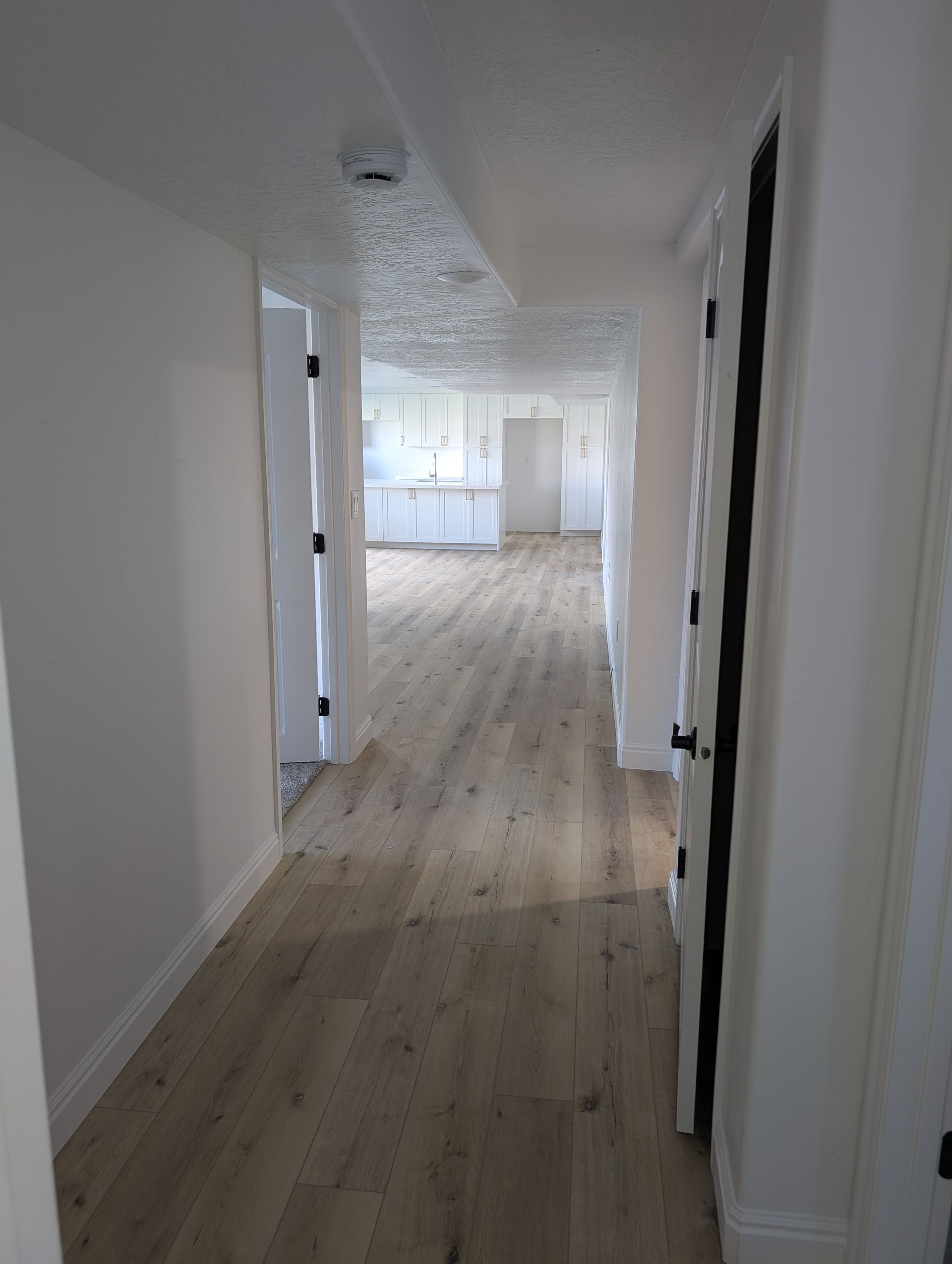 A long hallway with hardwood floors and white walls leading to a kitchen.