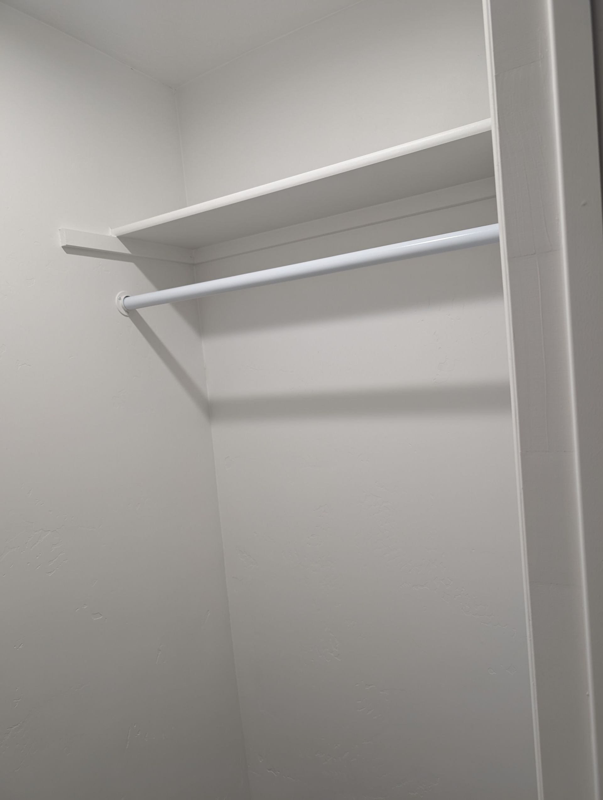 An empty closet with a shelf and clothes rack.