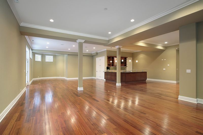 An empty basement with hardwood floors and a kitchen.