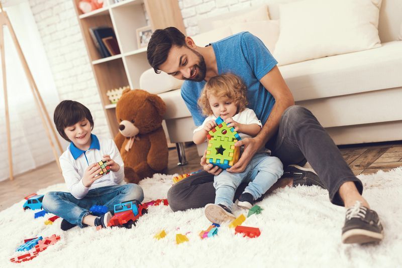 A man and two children are sitting on the floor playing with toys.