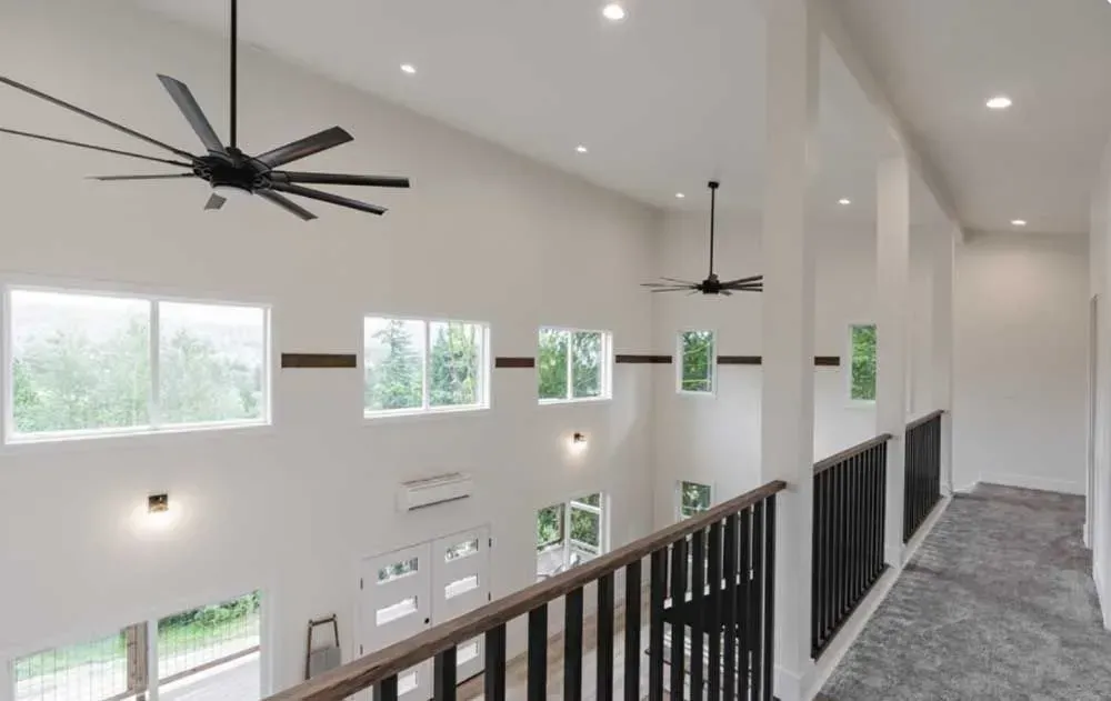 A large white room with a ceiling fan and a staircase
