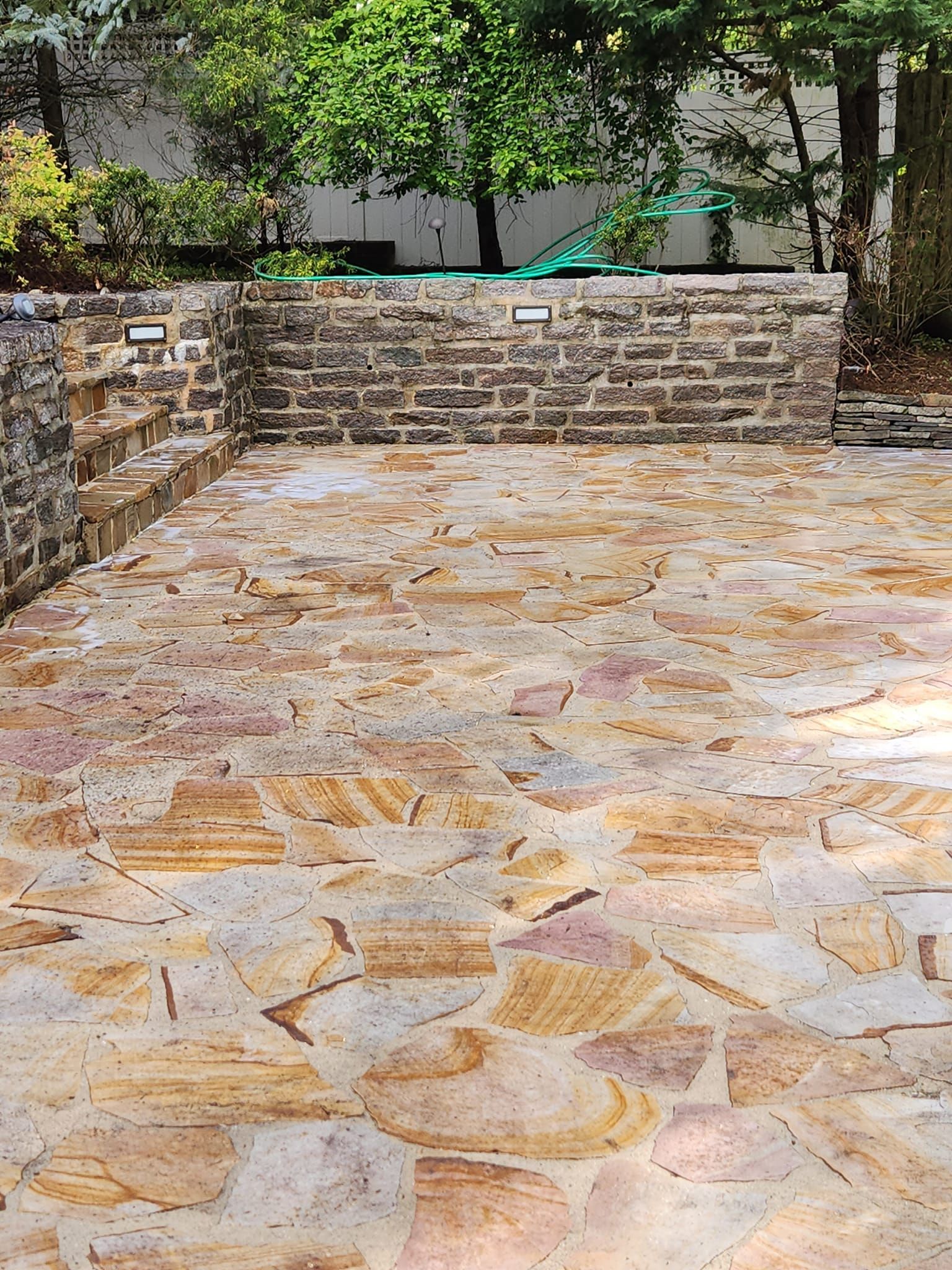 A stone patio with a brick wall and trees in the background.