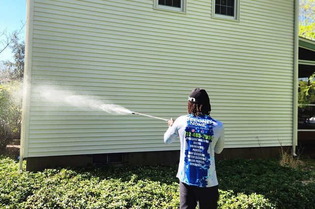 A man is cleaning the side of a house with a pressure washer.