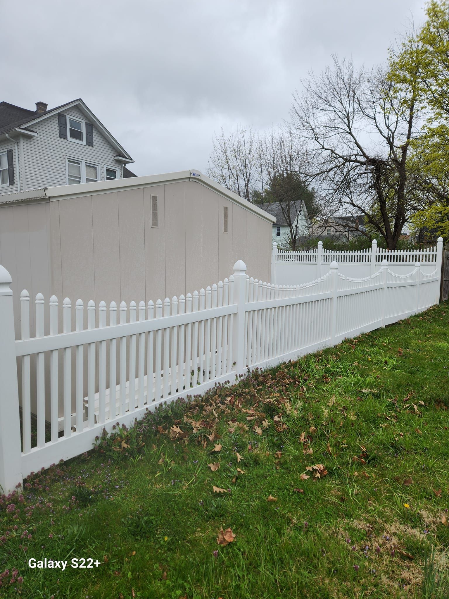 A white picket fence surrounds a grassy yard in front of a house.