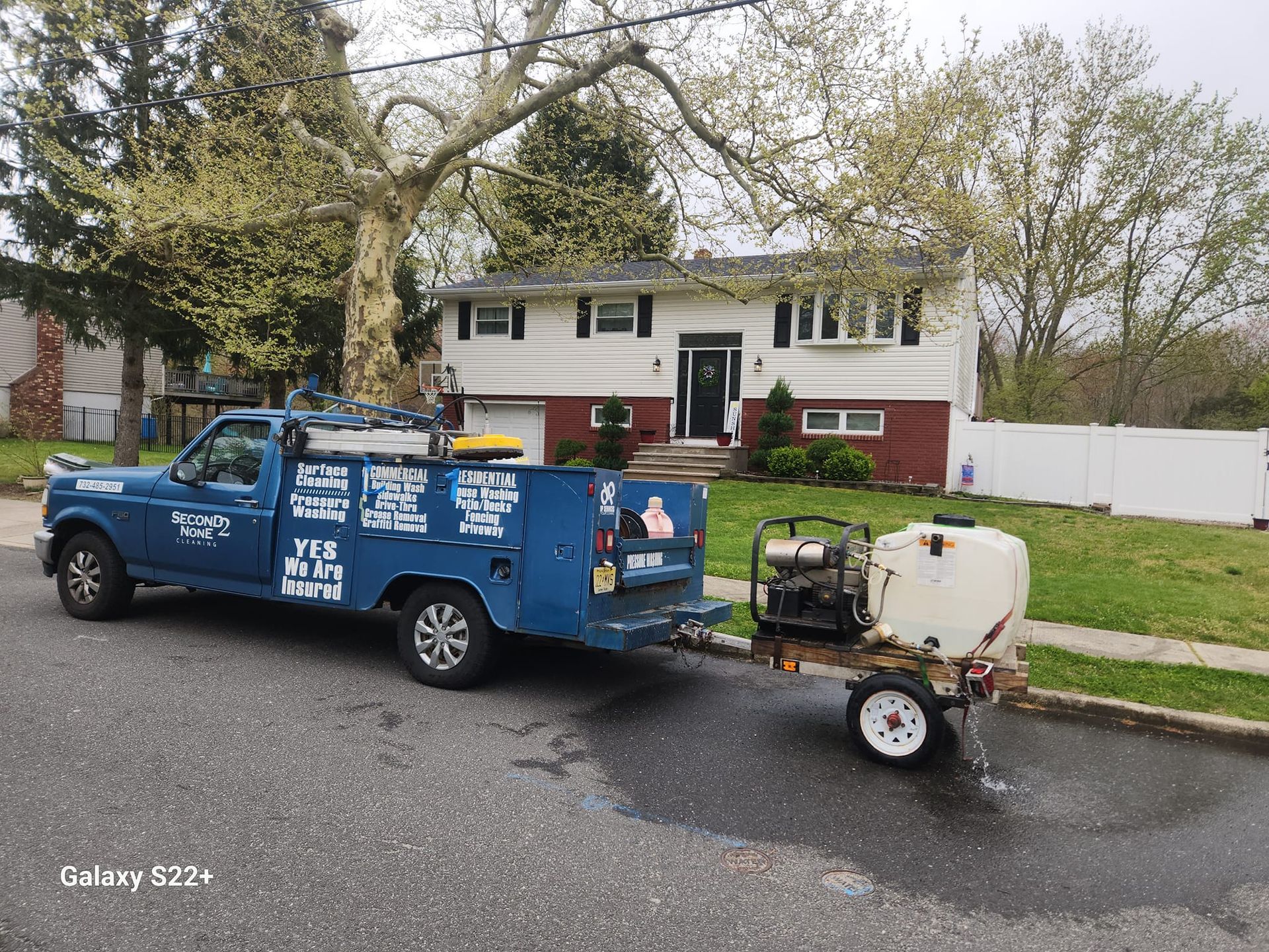 A blue truck with a trailer attached to it is parked in front of a house.