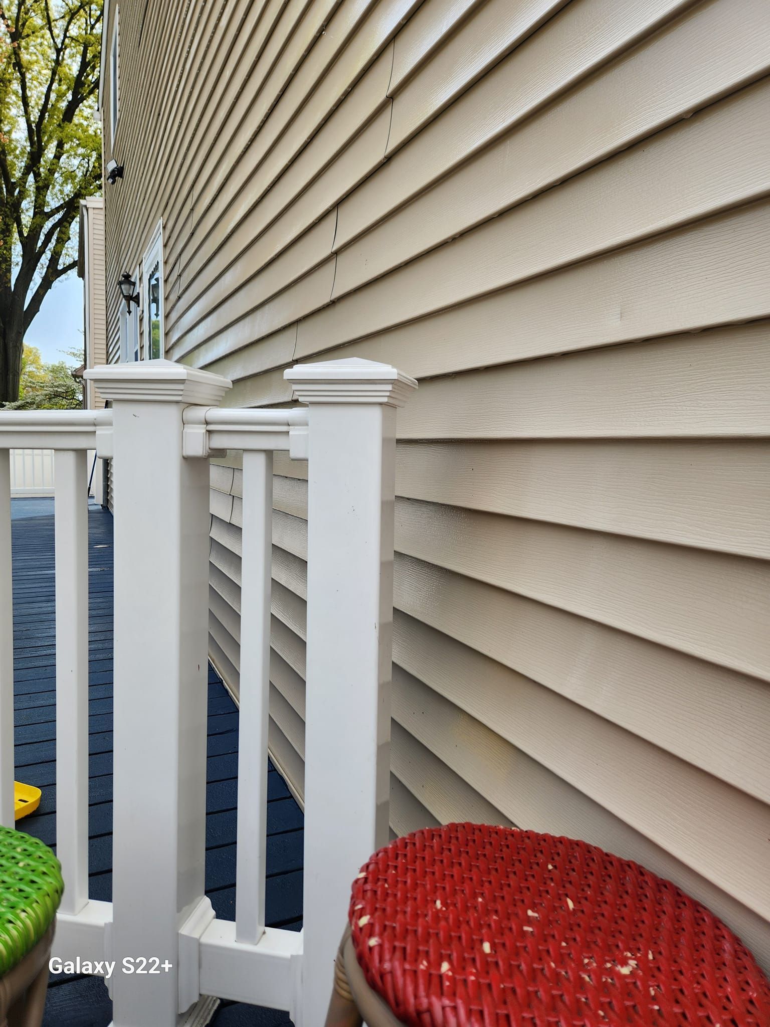 A white fence with a red cushion on a porch next to a house.