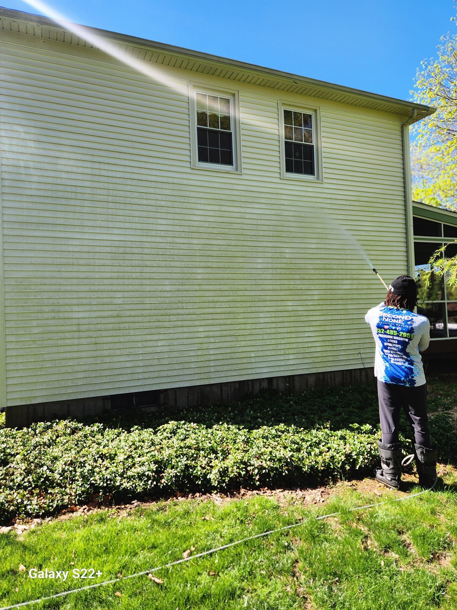A person is cleaning the side of a house with a pressure washer.