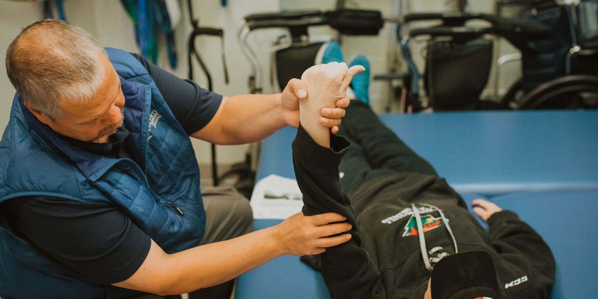 A man is stretching a person 's leg on a table.