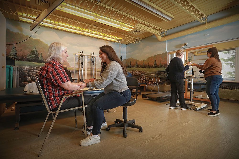 A woman is sitting at a table talking to an older woman in a therapy room.