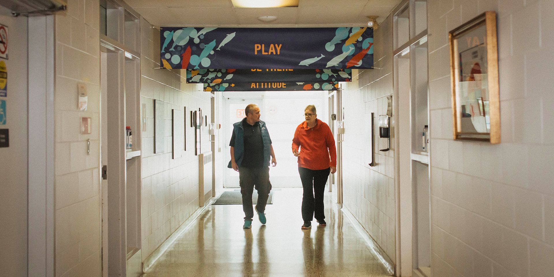 Two men are walking down a hallway in a building.