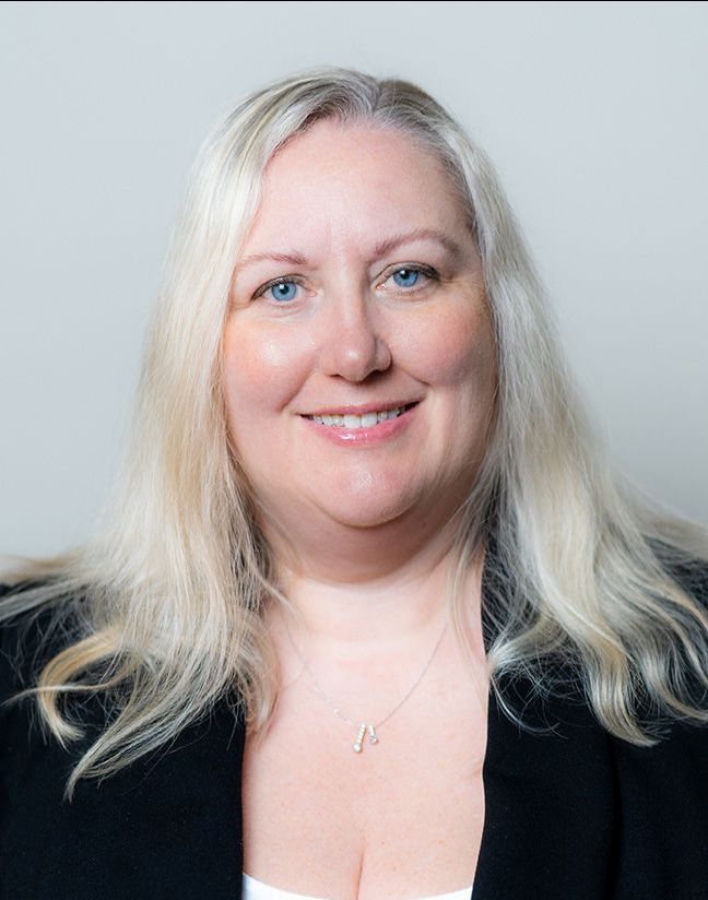 A woman with blonde hair and blue eyes is smiling for the camera