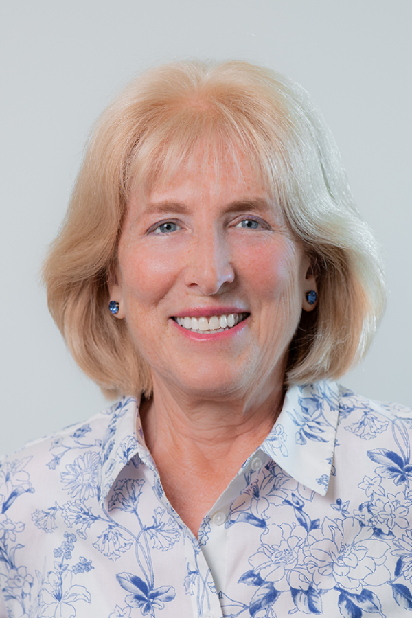 A woman in a blue shirt and black jacket smiles for the camera