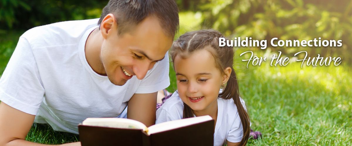 A man and a little girl laying on the grass reading a book