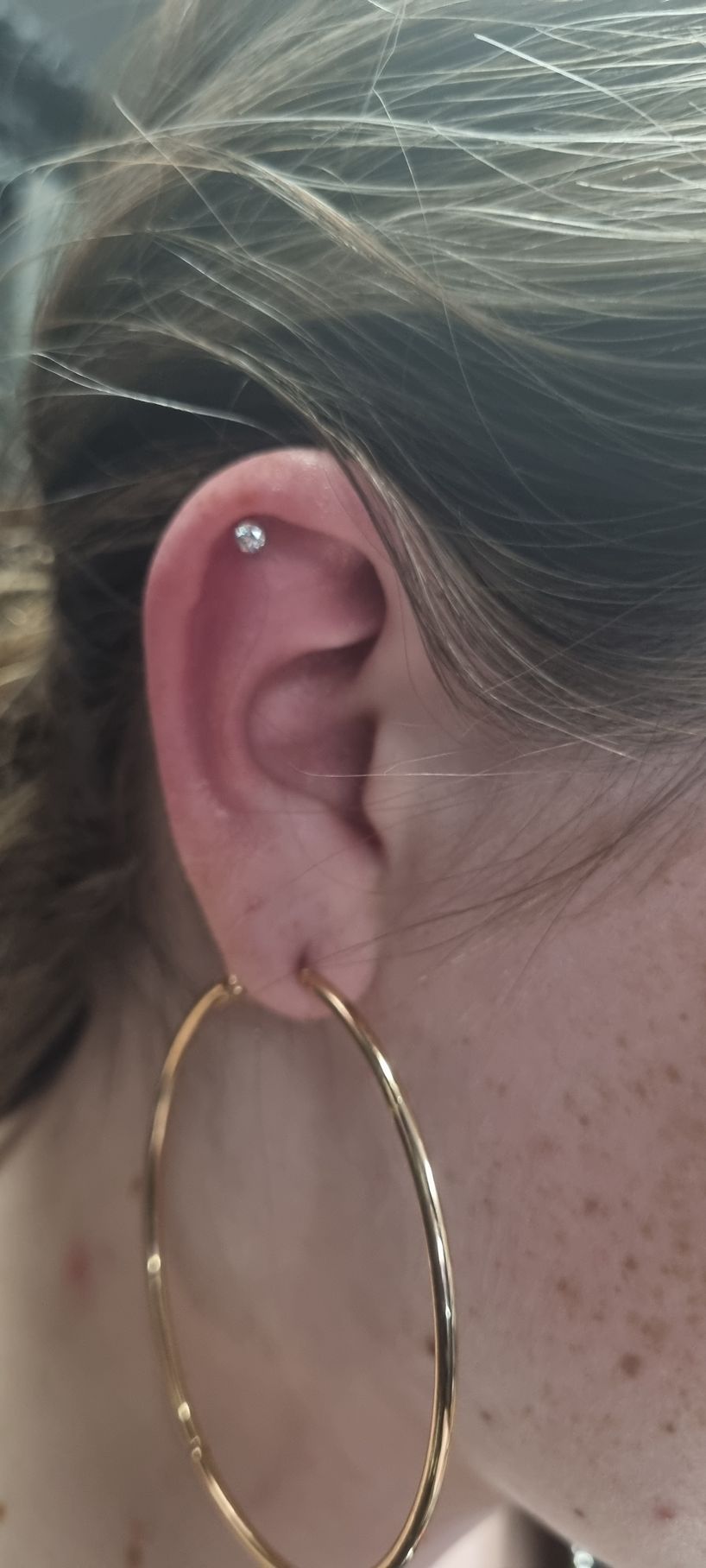 A close up of a woman 's ear with hoop earrings.