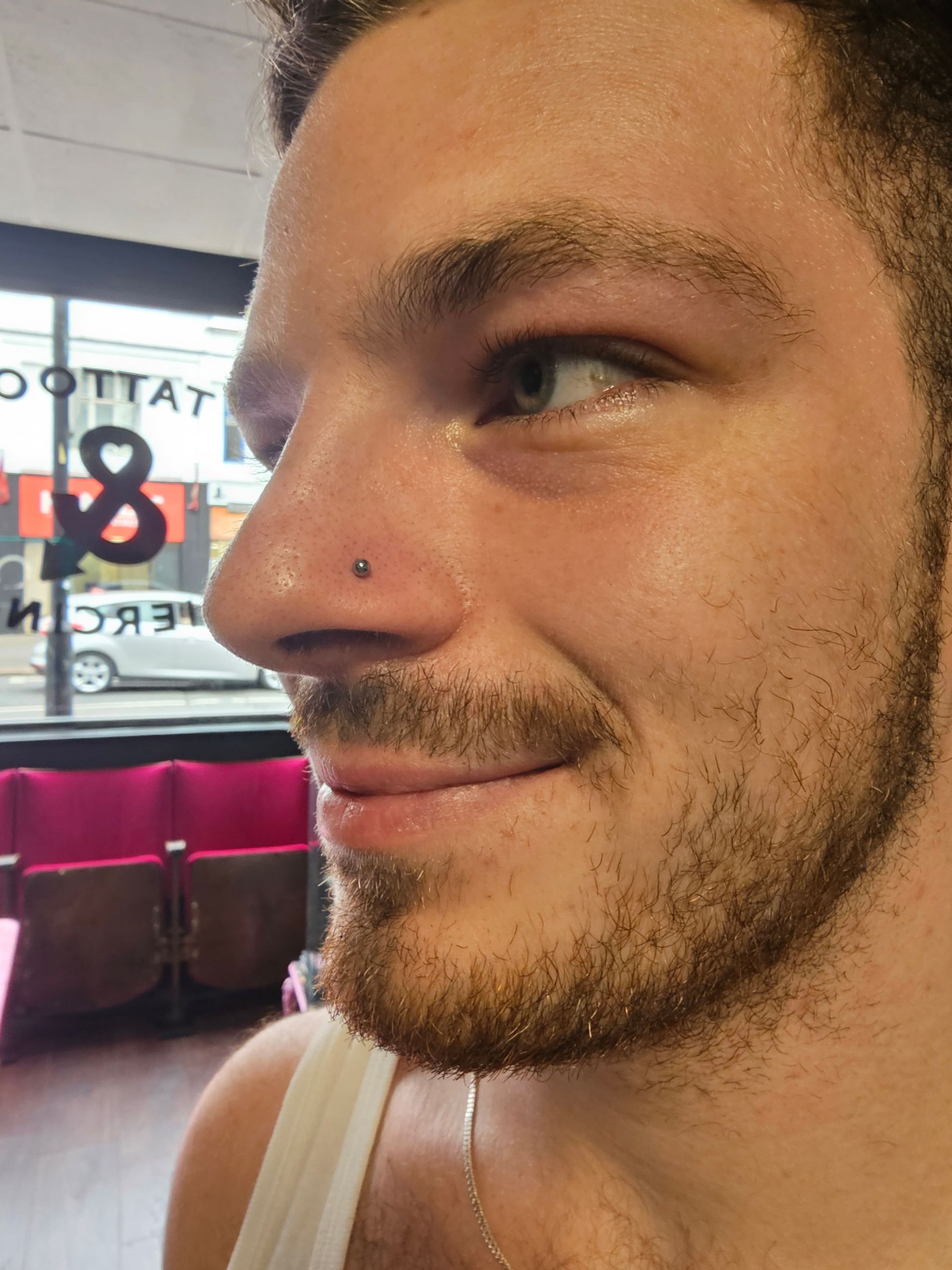 A man with a beard and a nose piercing is smiling.