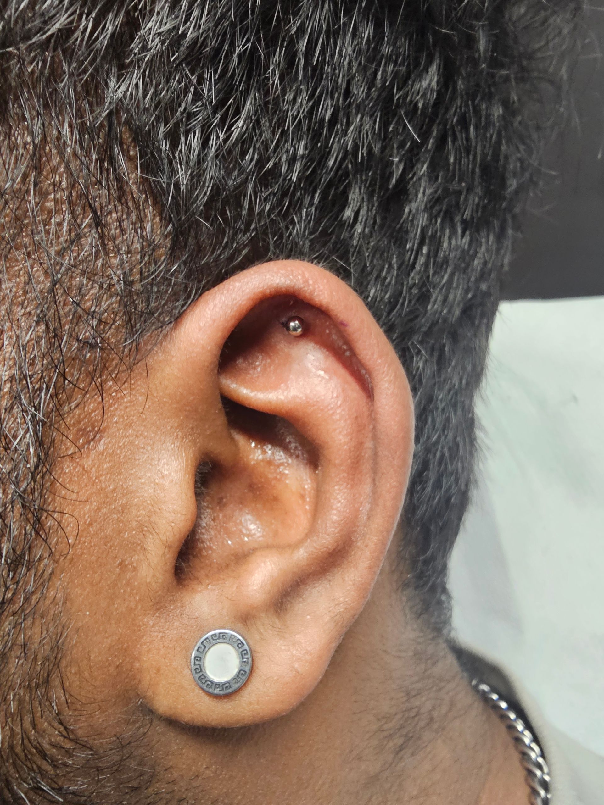 A close up of a man 's ear with a piercing and earrings.