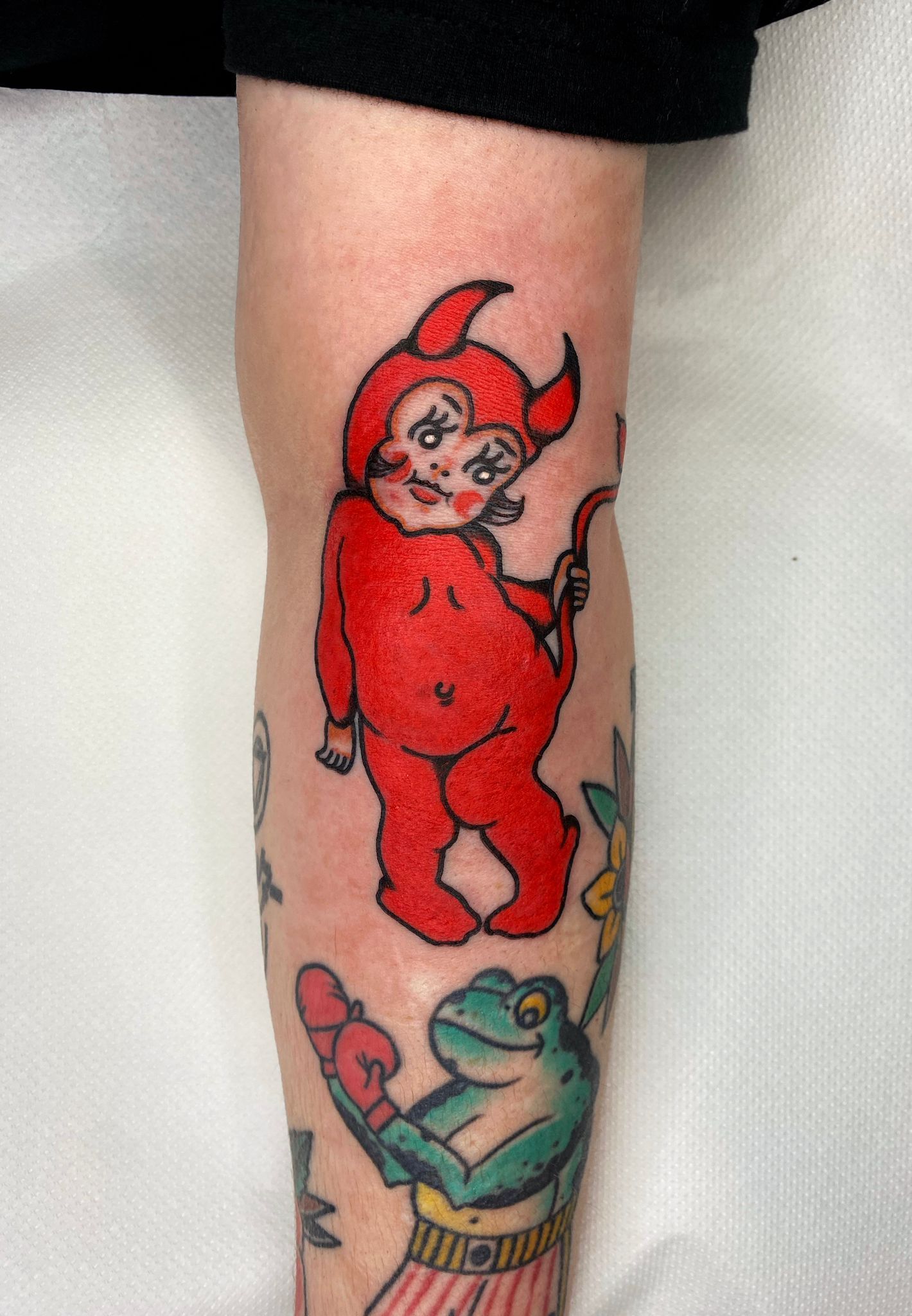 A person has a tattoo of a devil and a frog on their arm.