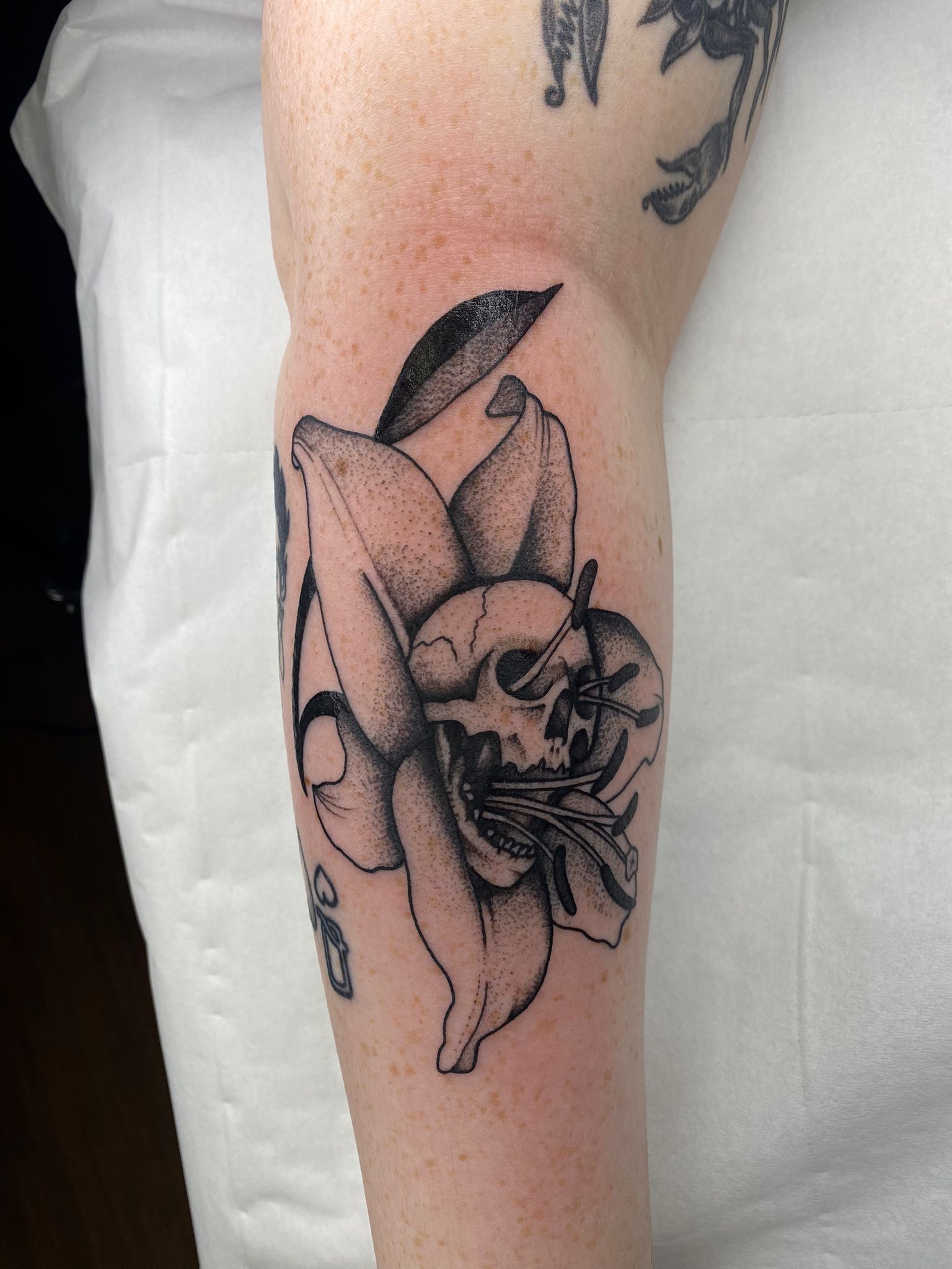 A black and white tattoo of a skull in a flower on a person 's arm.