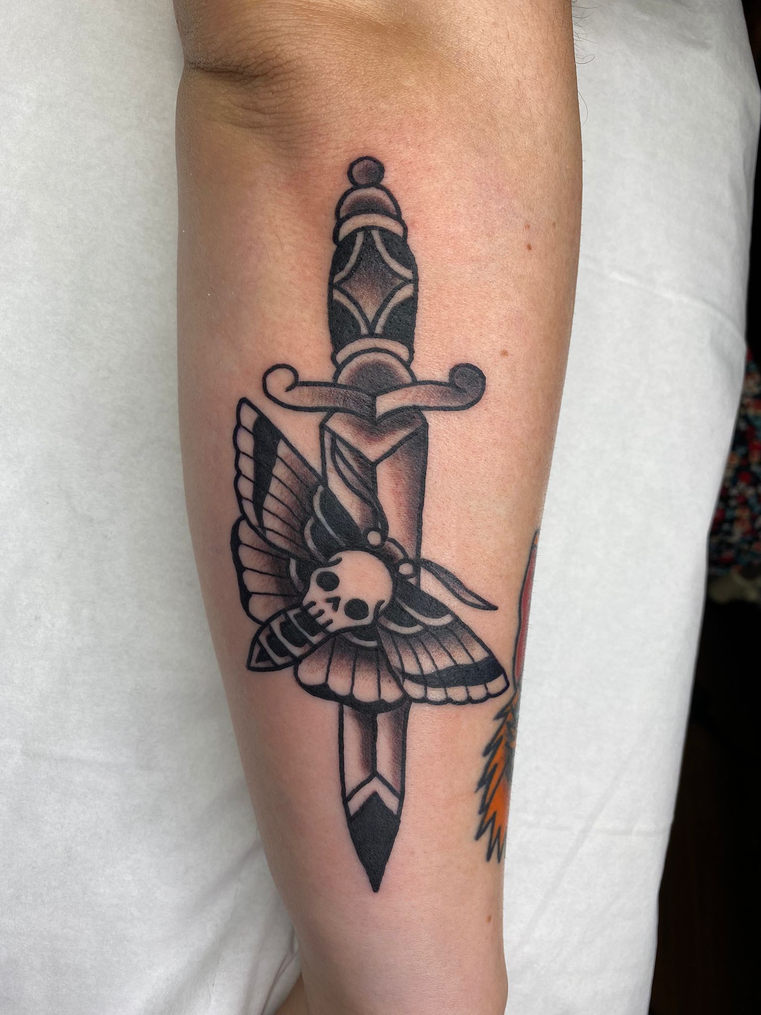A person has a tattoo of a dagger with a butterfly and a skull on it.