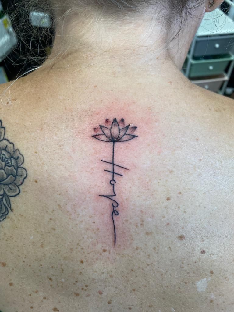 A woman has a tattoo of a lotus flower and the word hope on her back.