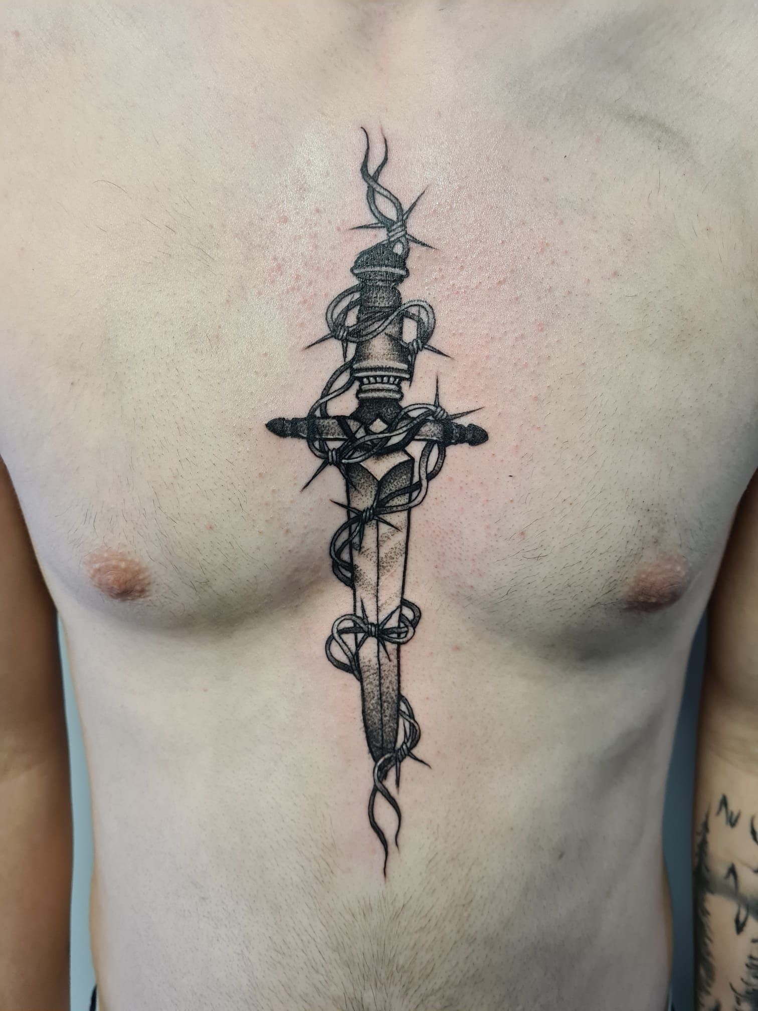 A man has a tattoo of a dagger with barbed wire around it