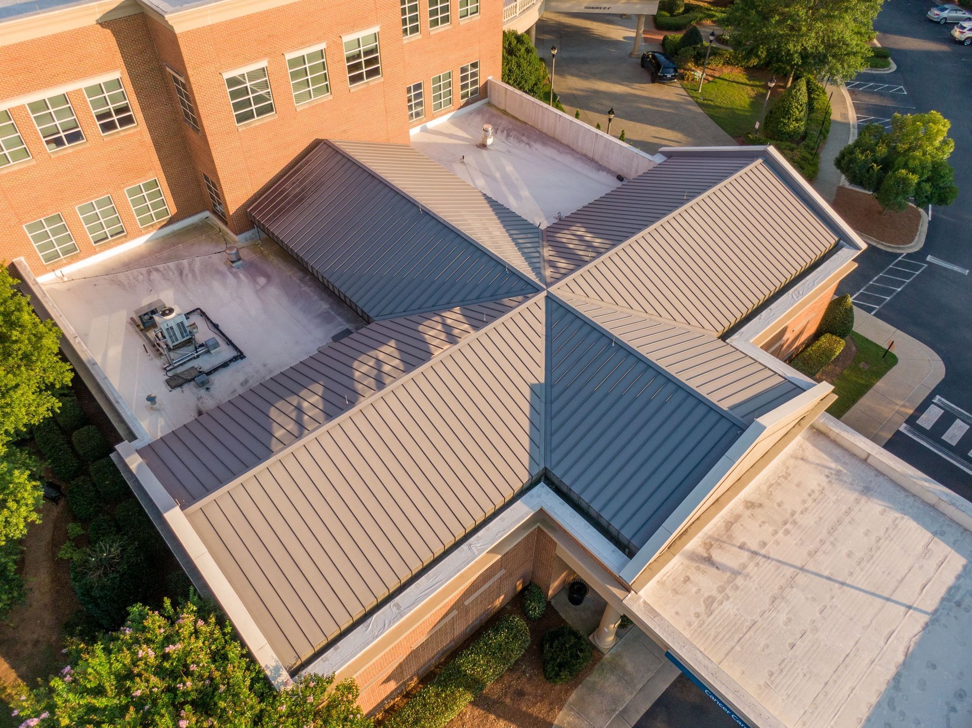 An aerial view of a brick building with a gray metal roof and flat white surfaces.