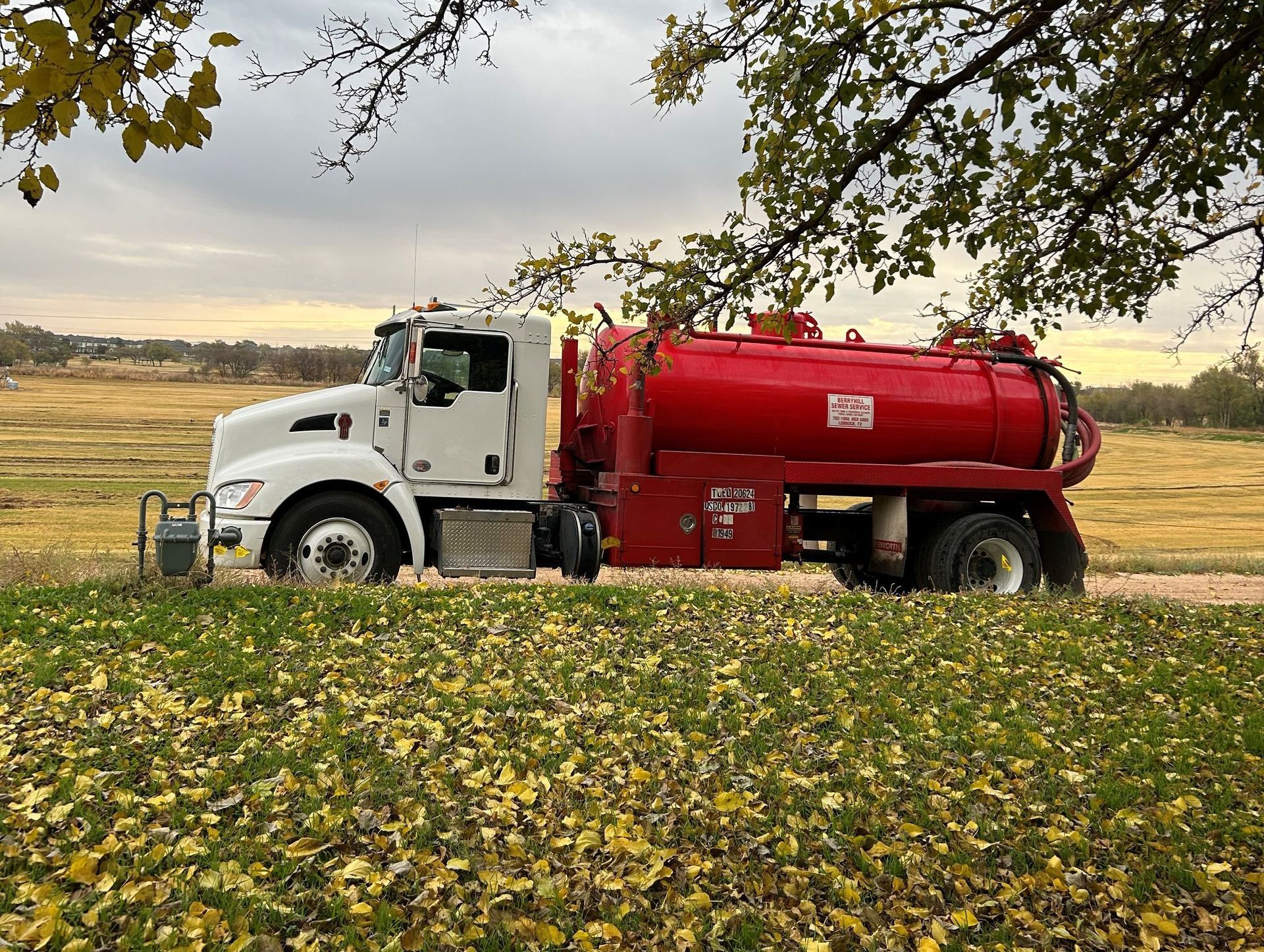 A Red Vacuum Truck is Parked in a Field with a Hose Attached to it — Lubbock, TX — Berryhill Sewer Inc.