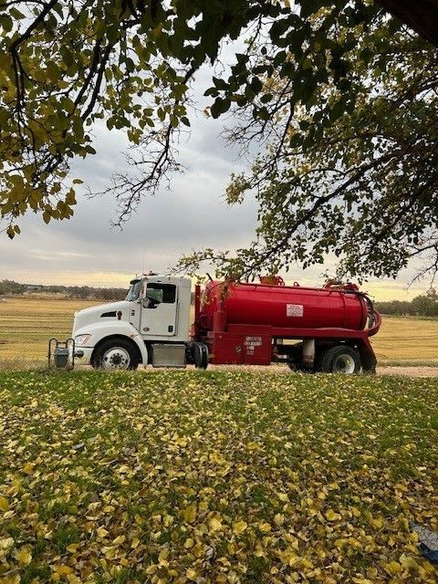 A Red Septic Tank Truck is Parked in a Field with Leaves on the Ground 